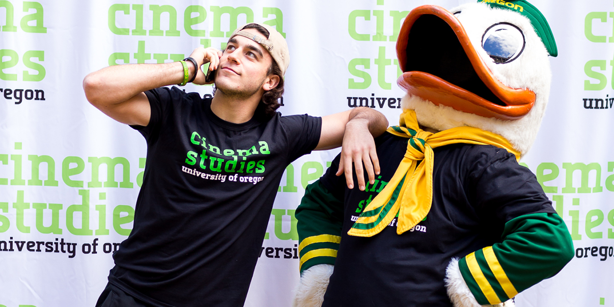 a student talking on a phone next to the UO Duck mascot